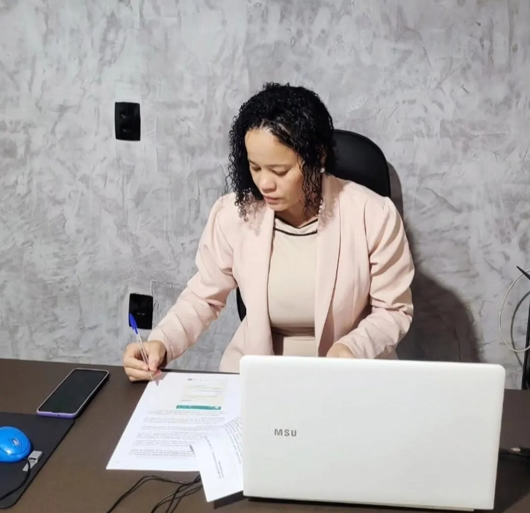 Dra. Marcela Paixão sentada em sua mesa de atendimento, analisando e assinando papéis do escritório
